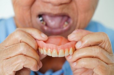 An elderly person holding a removable denture
