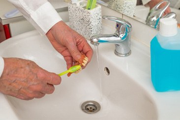 An old man brushing a denture with a toothbrush