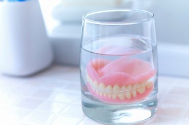 : A closeup of dentures soaking in a glass