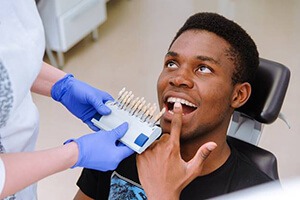 man pointing to teeth with whitening shade chart