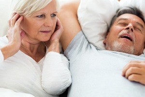 woman covering ears while husband snores