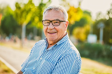 Older man with glasses smiling with dental implants in Northampton, MA