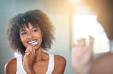 A young woman brushing her teeth in front of a bathroom mirror