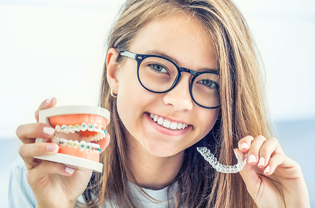 girl holding teeth with braces and an invisalign tray