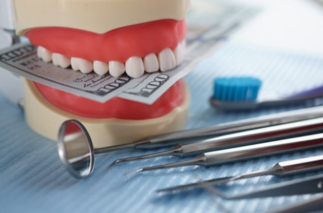 Artificial jaw mockup with money and dental instrument on table