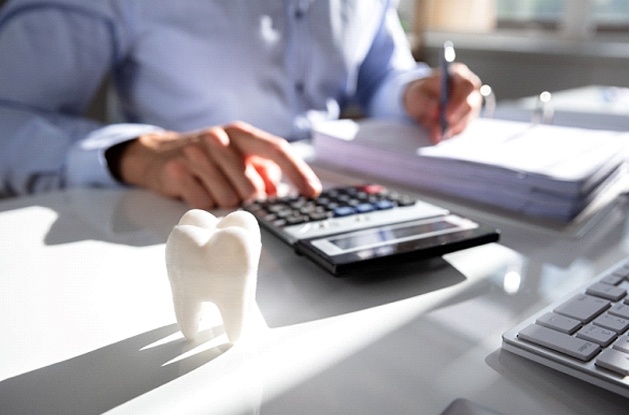 Person using calculator next to prosthetic tooth