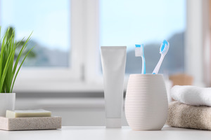 Two toothbrushes in holder on counter next to toothpaste tube and towels